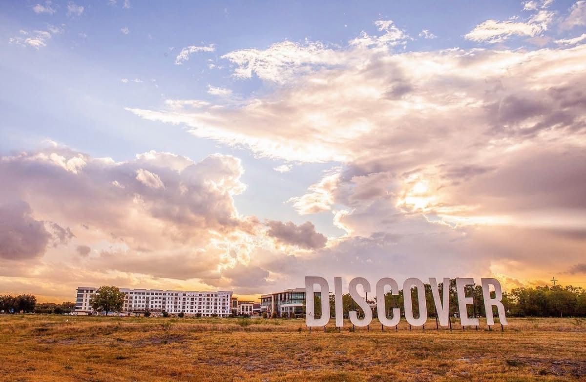 Large white DISCOVER letters standing in an open field at Clearfork under a sunset sky